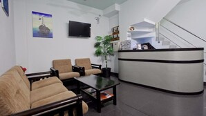 A reception area with a reception desk, a flat-screen TV, a potted plant, and a staircase. - Kaani Lodge (Malé)