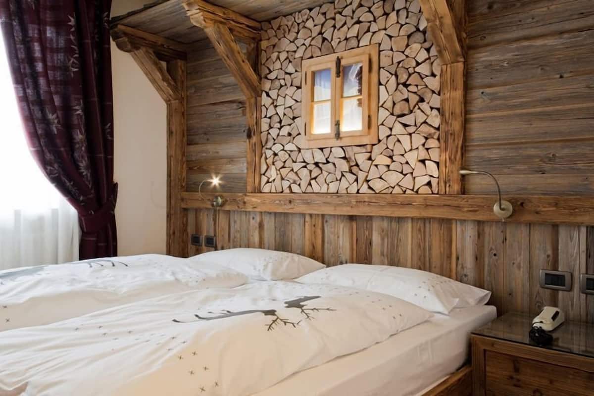A wooden cabin-style bedroom with a bed, a nightstand, and a wall-mounted lamp.