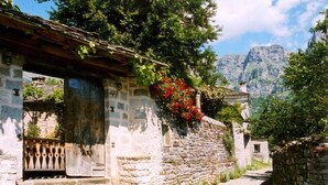 Um edifício de pedra com porta de madeira e degraus que levam a ele, rodeado por vegetação e uma montanha ao fundo.