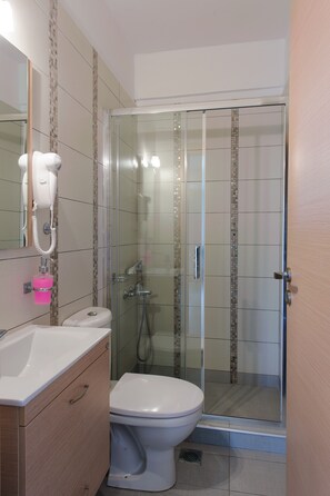Ein Badezimmer mit Toilette, Waschbecken, Fön und Duschkabine.