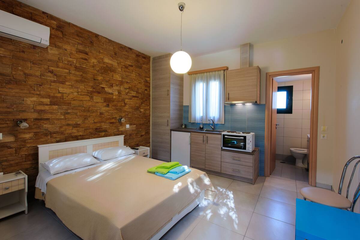 Une chambre avec un mur en bois, un lit recouvert de draps blancs, une table de chevet et une commode.