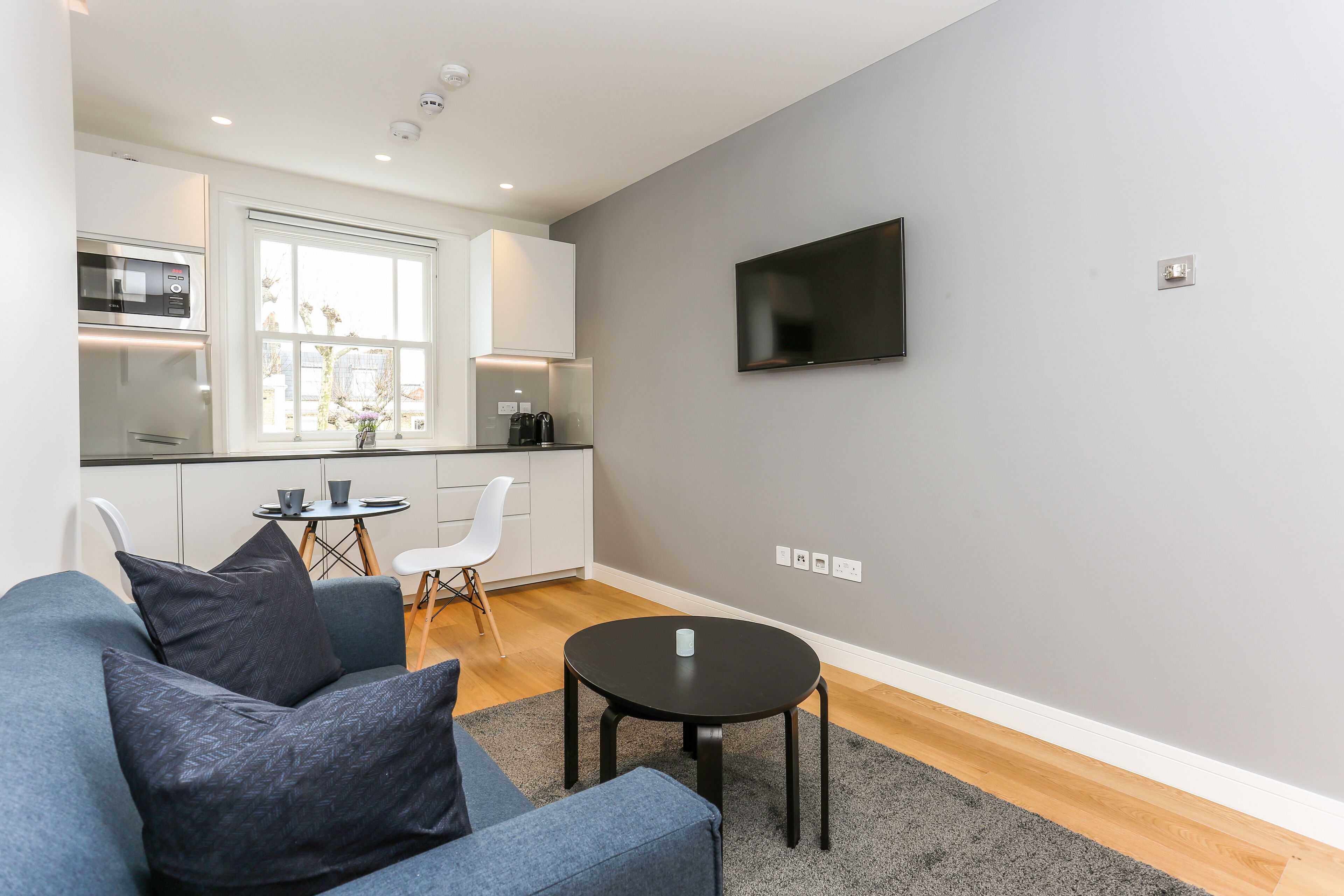 Ein modernes Wohnzimmer mit einem grauen Sofa, einem kleinen runden Tisch und einem flachbildfernseher, der an der Wand befestigt ist.