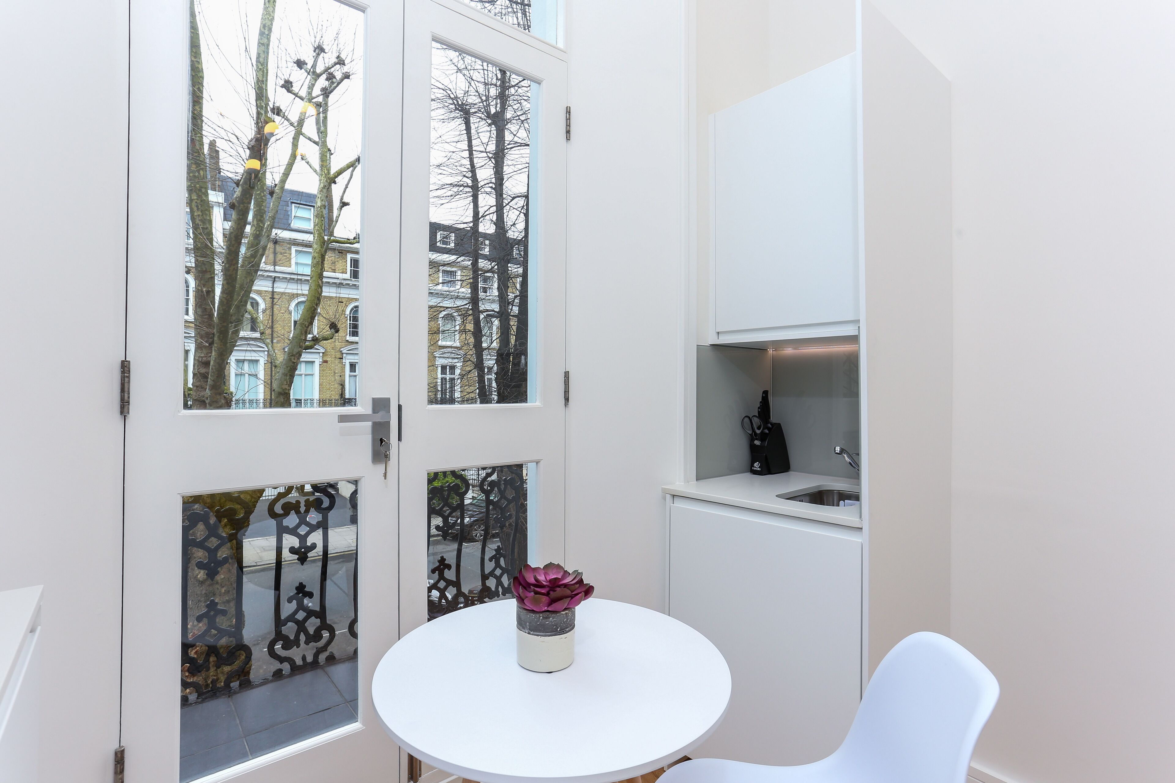 A compact room with a white door, a small table with a vase, and a white chair.