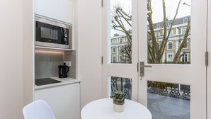 A compact kitchen with a microwave, a coffee maker, and a small potted plant on a white table. - Inverness Terrace Serviced Apartments by Concept Apartments (London)
