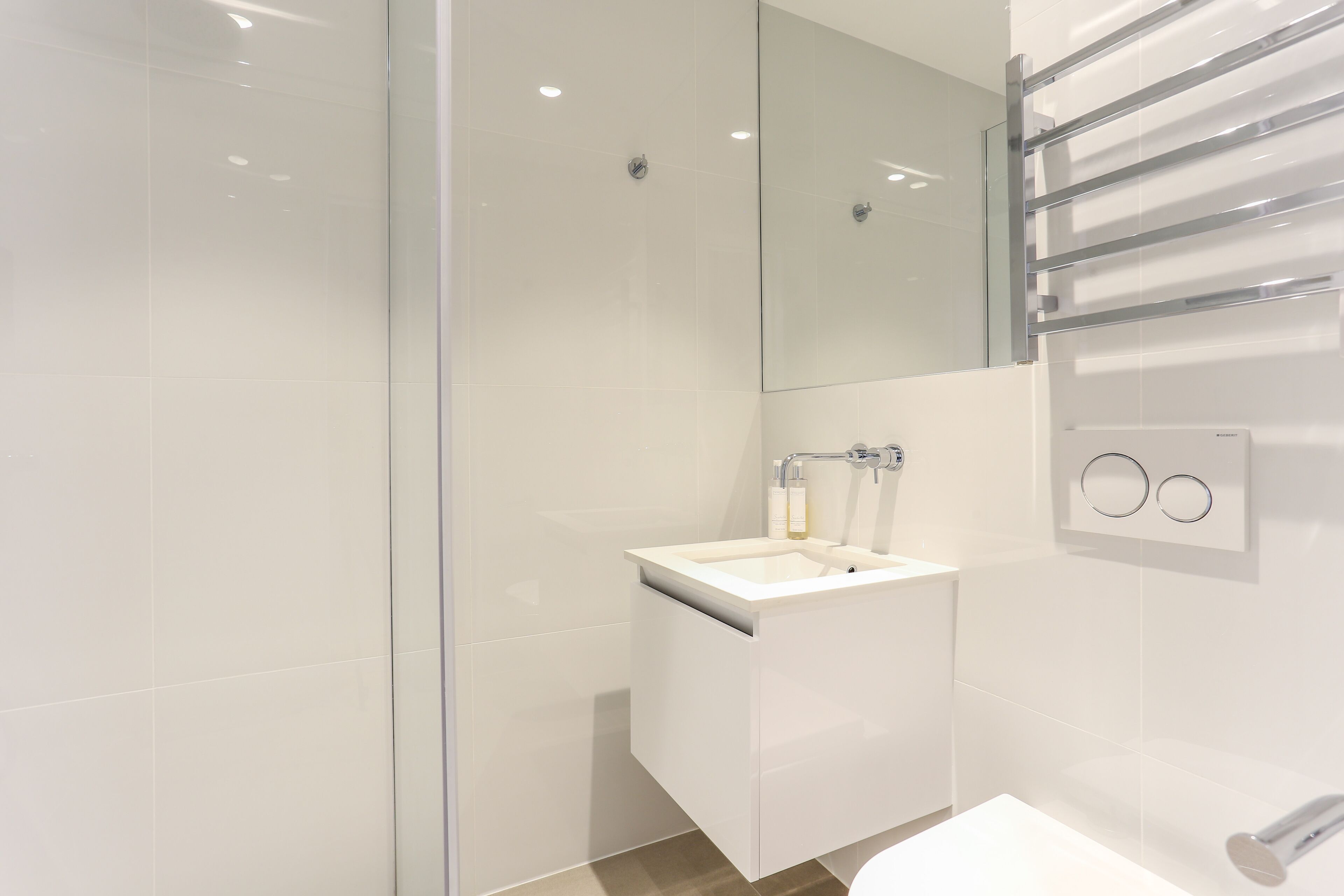 Un bany modern amb plat de dutxa de vidre, un lavabo blanc amb mirall a sobre i una barra de tovalloles a la paret.