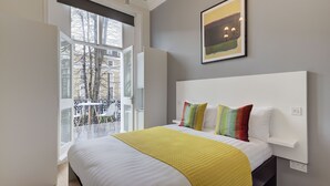 A modern bedroom with a large bed, a balcony with a view of buildings, and a painting on the wall. - Inverness Terrace Serviced Apartments by Concept Apartments (London)