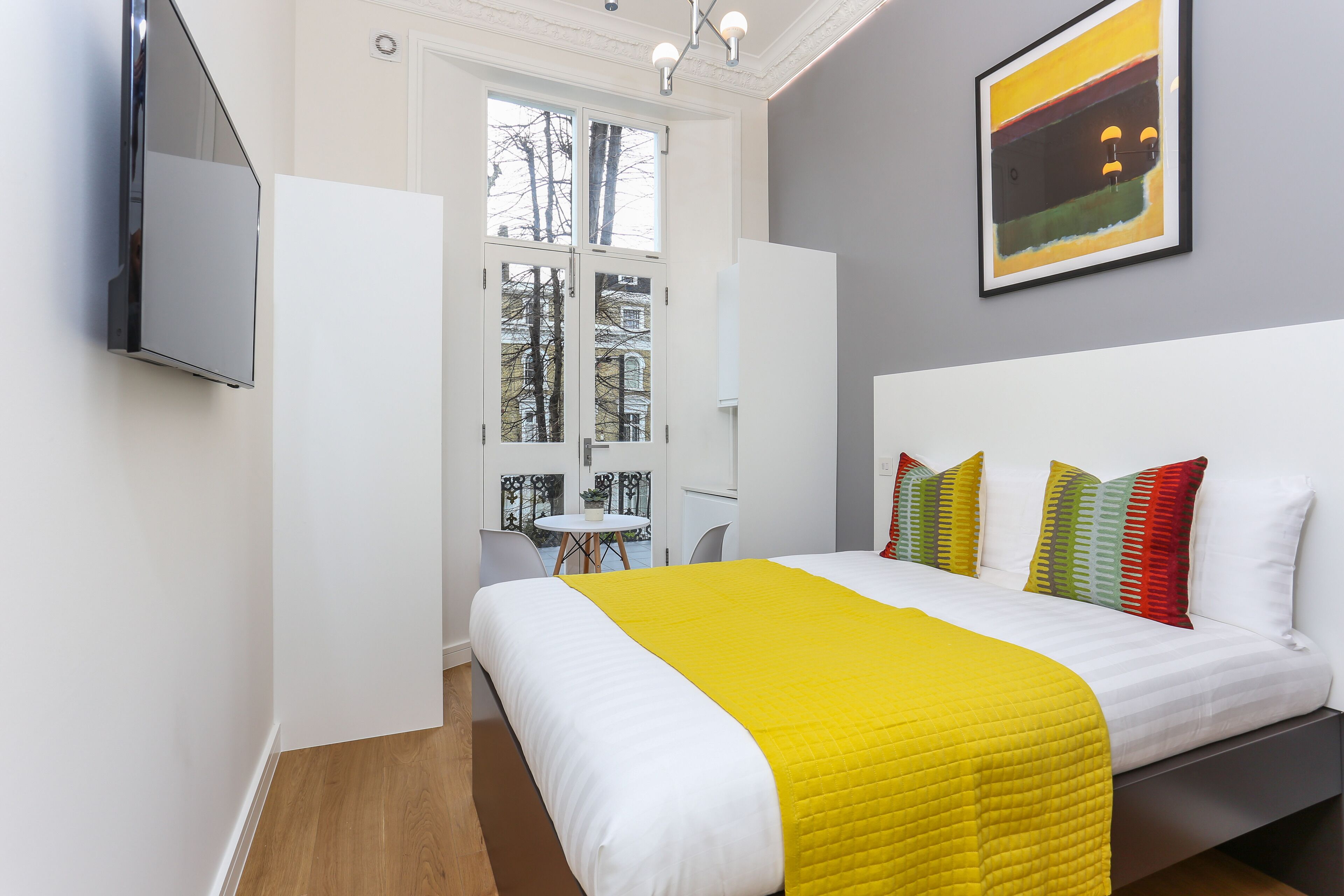 A modern hotel room with a large bed, a TV mounted on the wall, and a window with a view of trees and a building.