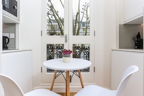 A room with a white round table, two white chairs, a potted plant, and a view through a glass door. - Inverness Terrace Serviced Apartments by Concept Apartments (London)