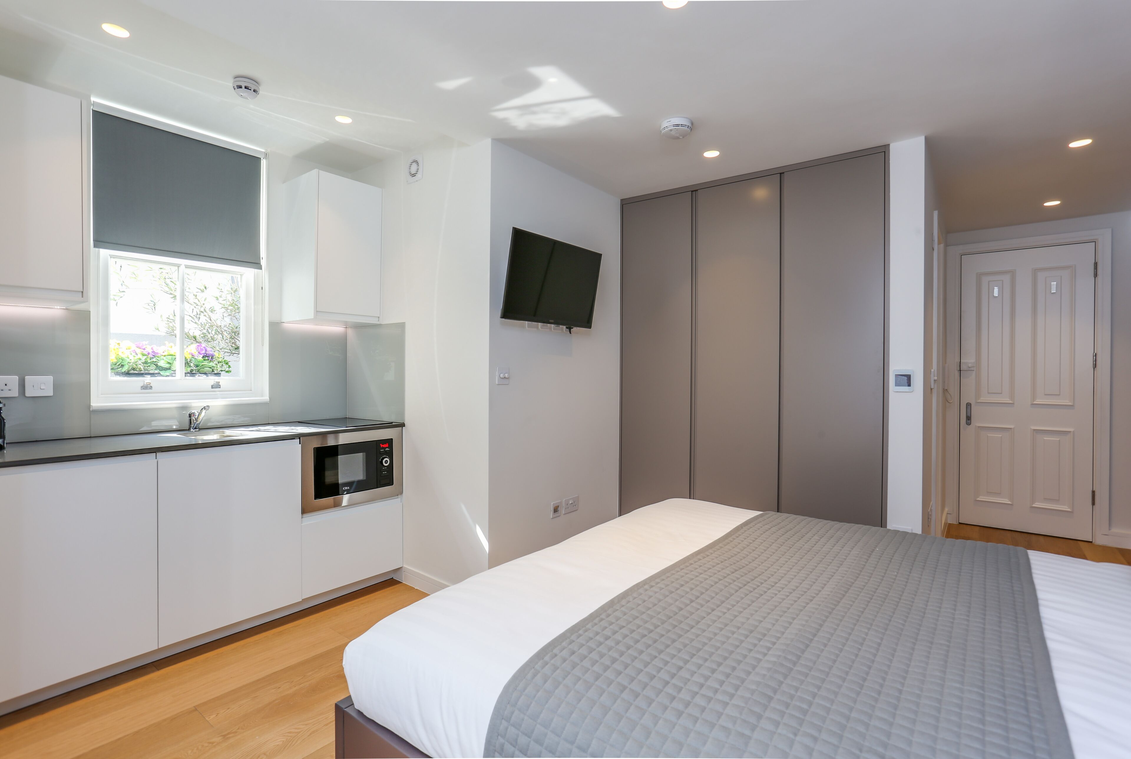 A modern bedroom with a large bed, a built-in TV, and a separate kitchenette area.