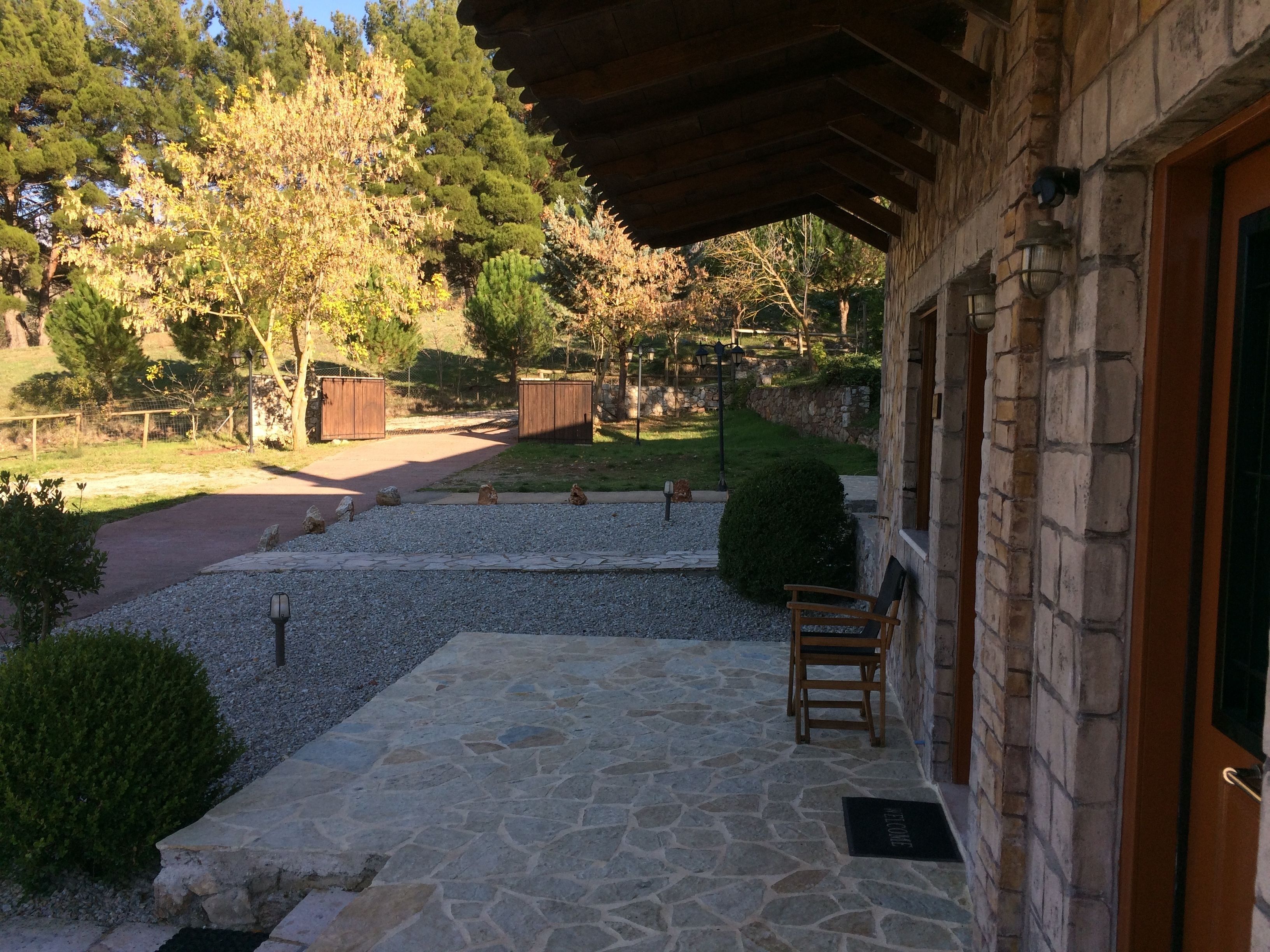 Une terrasse dallée de pierres, avec une chaise en bois, un mur de pierres et une vue sur une zone boisée.