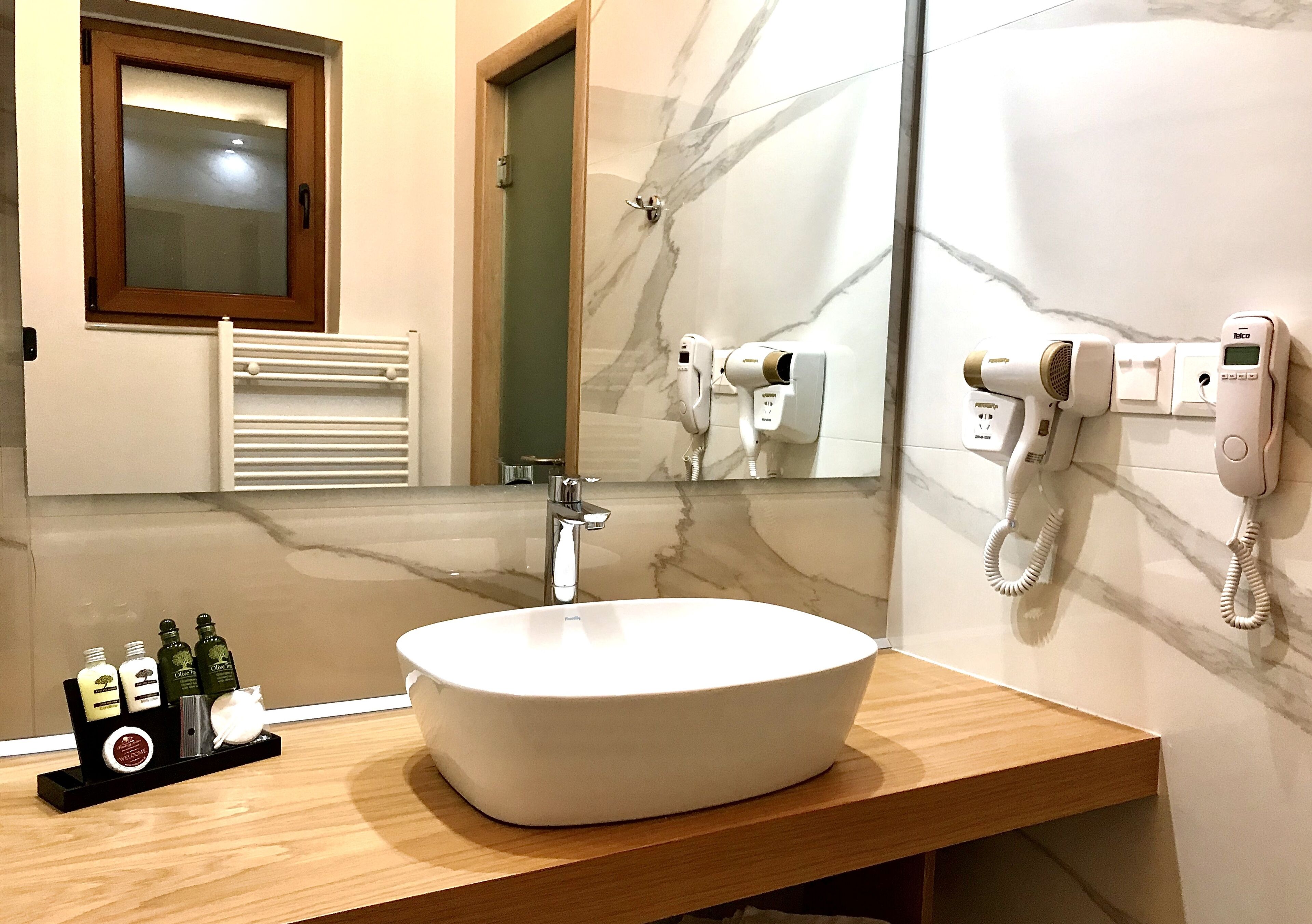 A bathroom with a white sink, a mirror, a towel rack, and two hair dryers mounted on the wall.