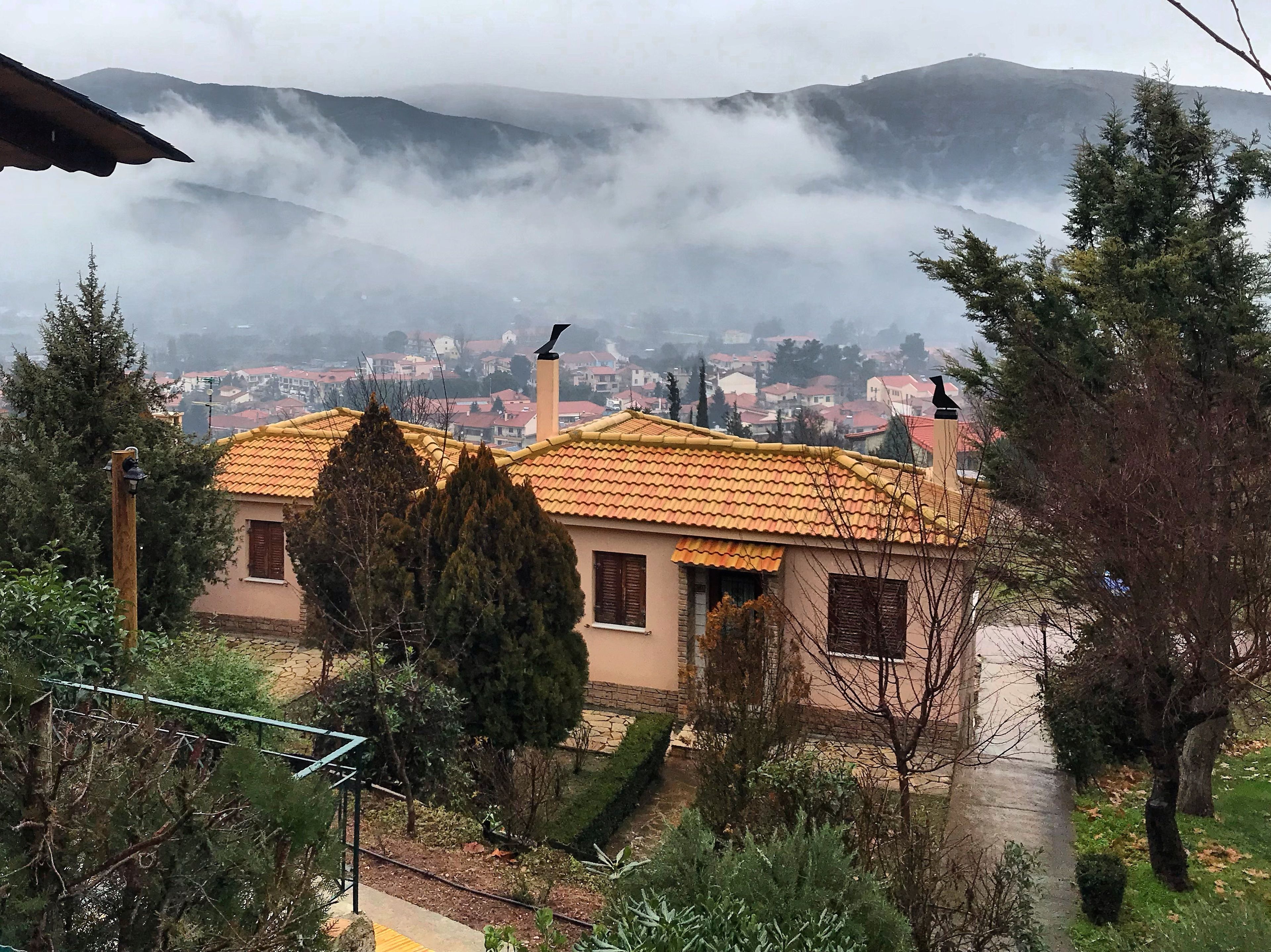 Una casa con techo de tejas, rodeada de árboles y con vista a un pueblo al fondo.