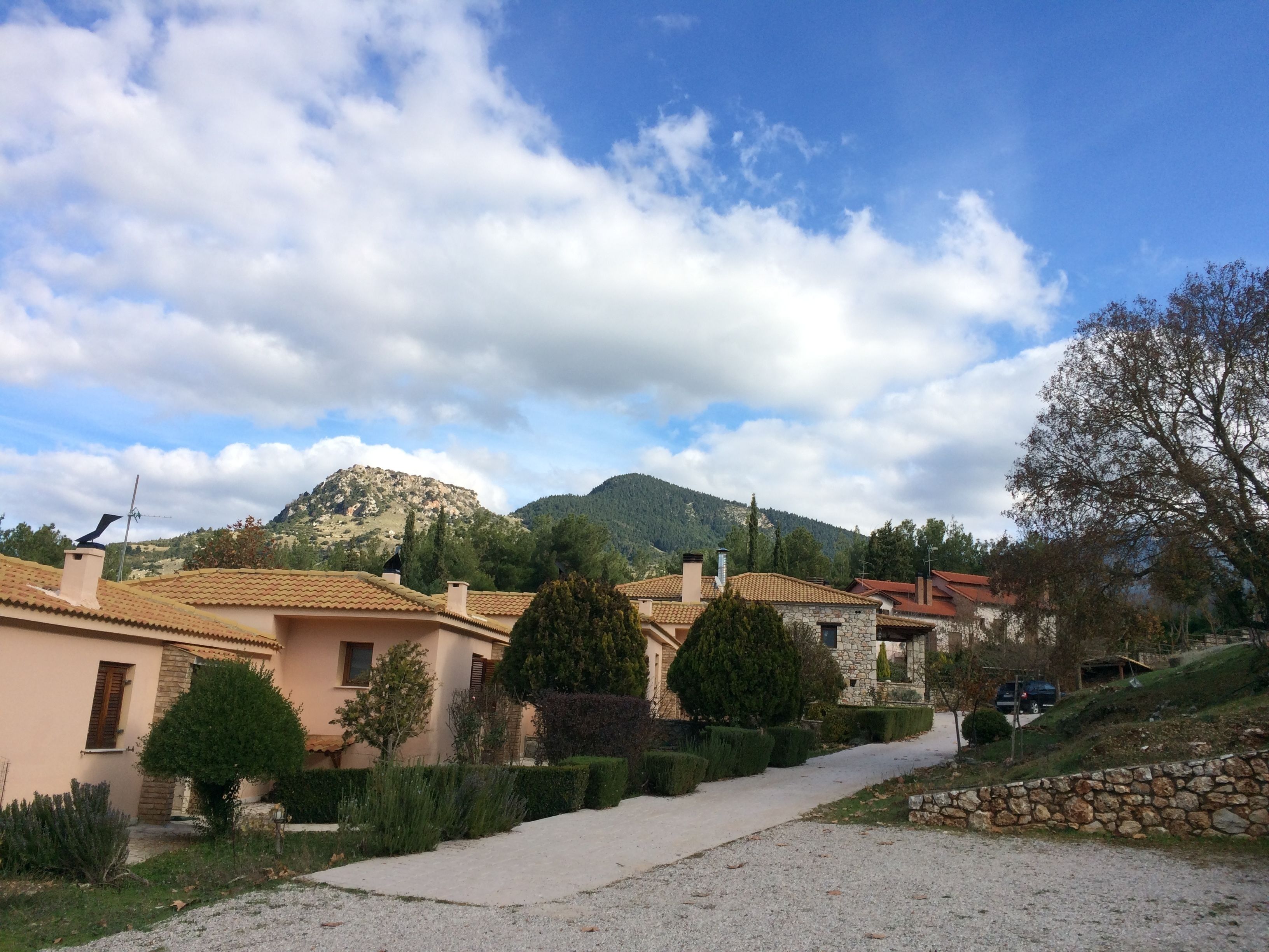 Un pueblo rural con casas de piedra, un camino de grava y una montaña al fondo.