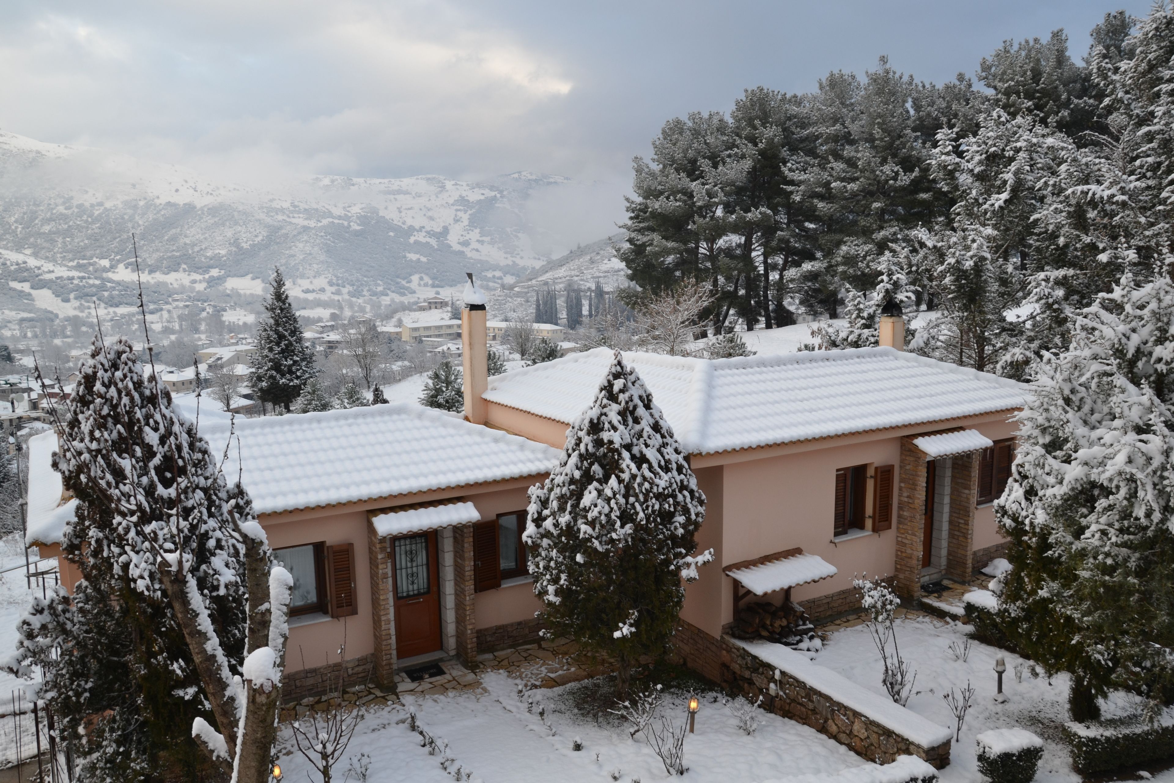 Una casa cubierta de nieve con fachada de piedra, puerta de madera y un pequeño jardín.
