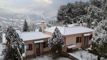Una casa cubierta de nieve con fachada de piedra, puerta de madera y un pequeño jardín.