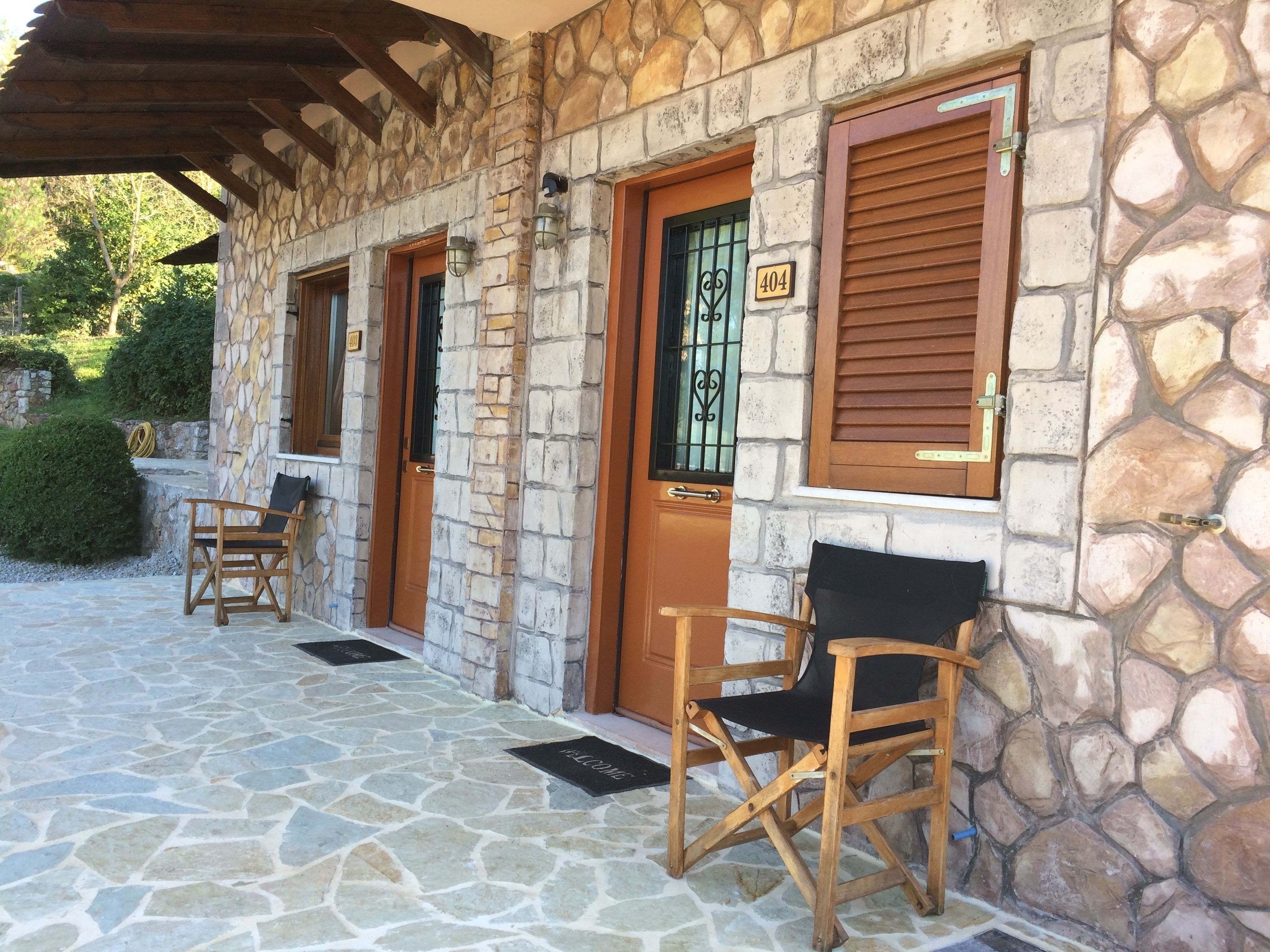 A stone building with three wooden doors, numbered 404, 405, and 406. There are two wooden chairs outside the doors.