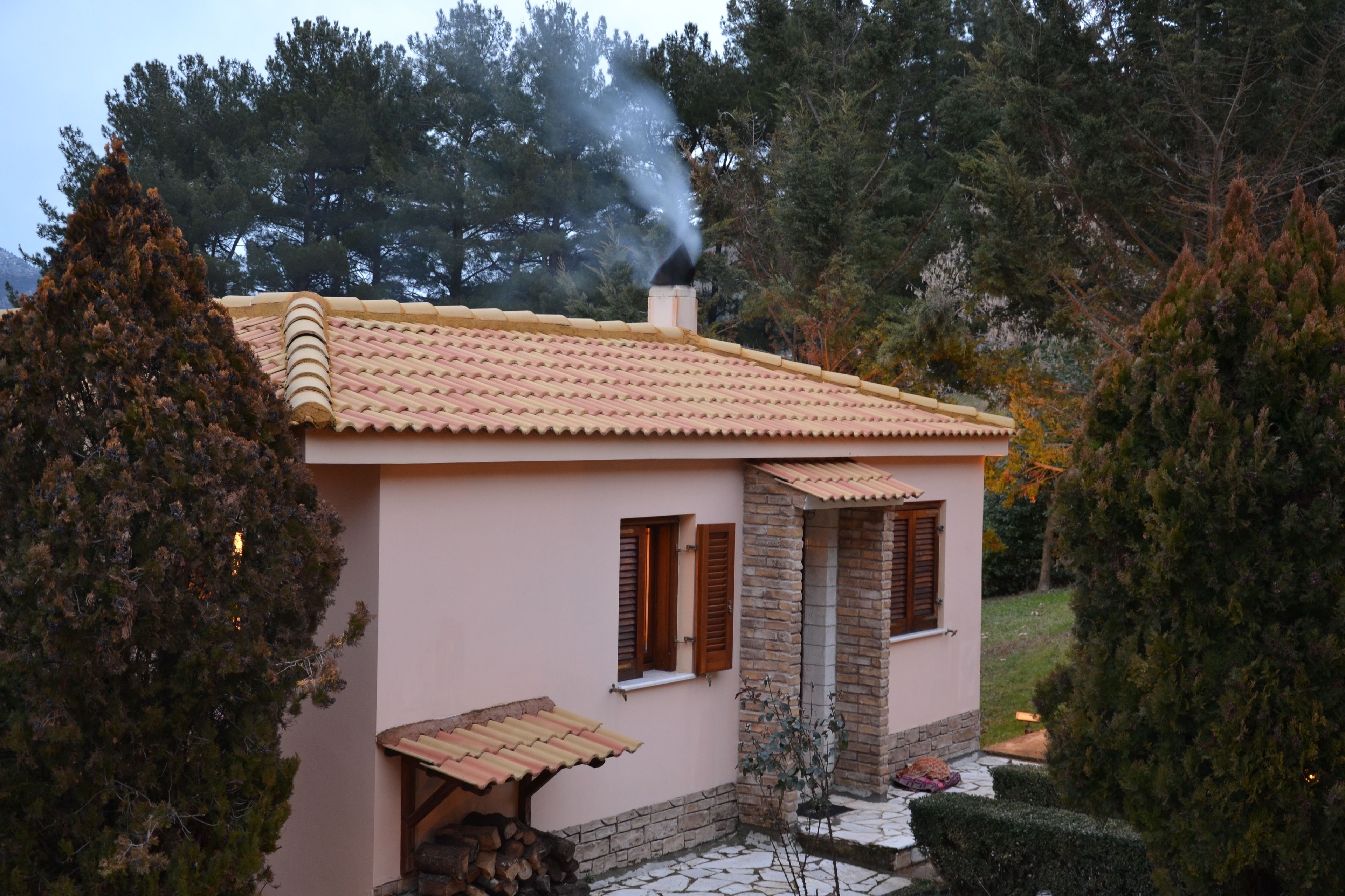 Una casa con techo de tejas, una chimenea y un pequeño porche con una mesa y sillas de madera.