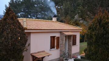 Una casa con techo de tejas, una chimenea y un pequeño porche con una mesa y sillas de madera.