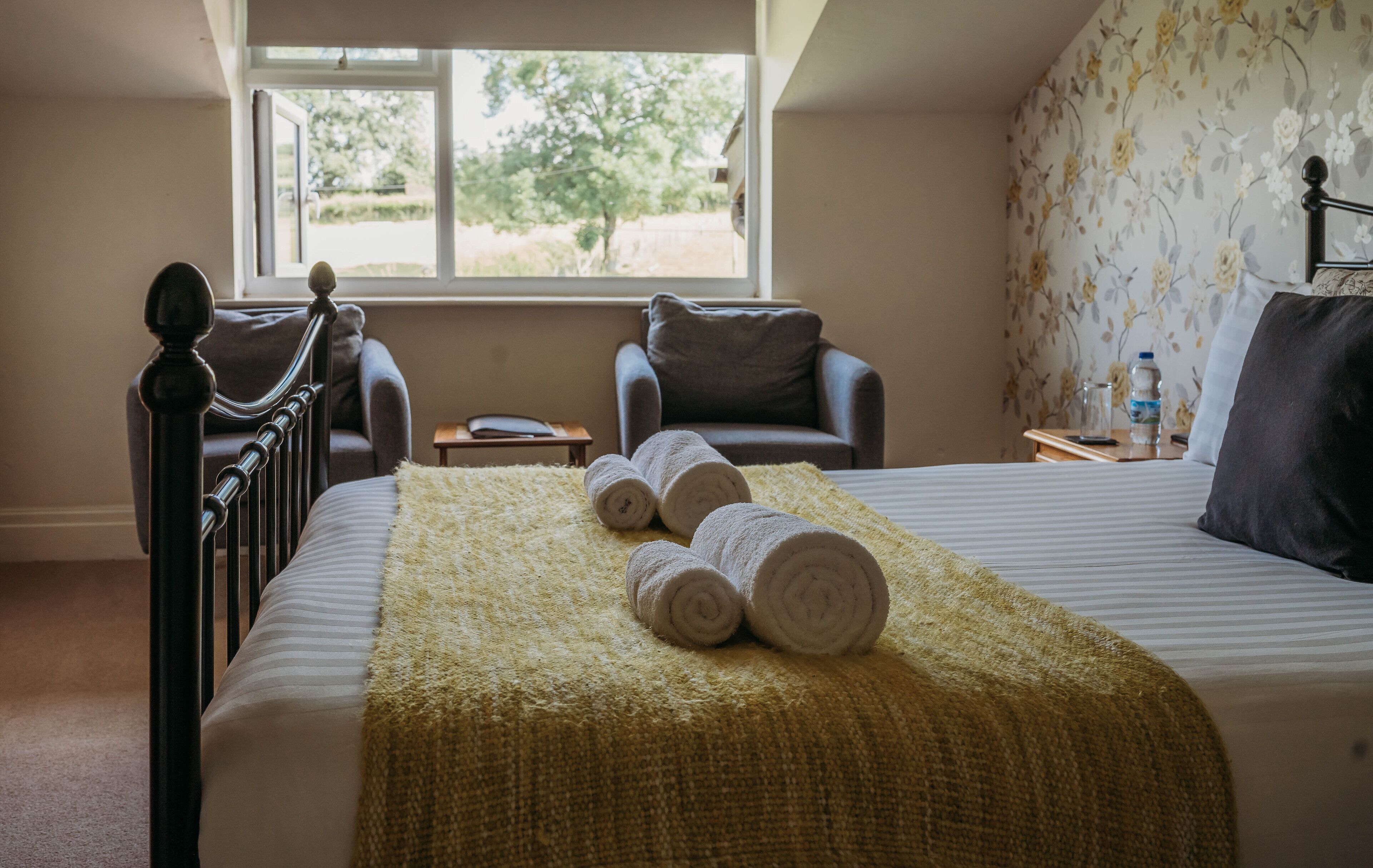 A bedroom with a bed, two chairs, a window, and a view of greenery outside.