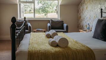 A bedroom with a bed, two chairs, a window, and a view of greenery outside.