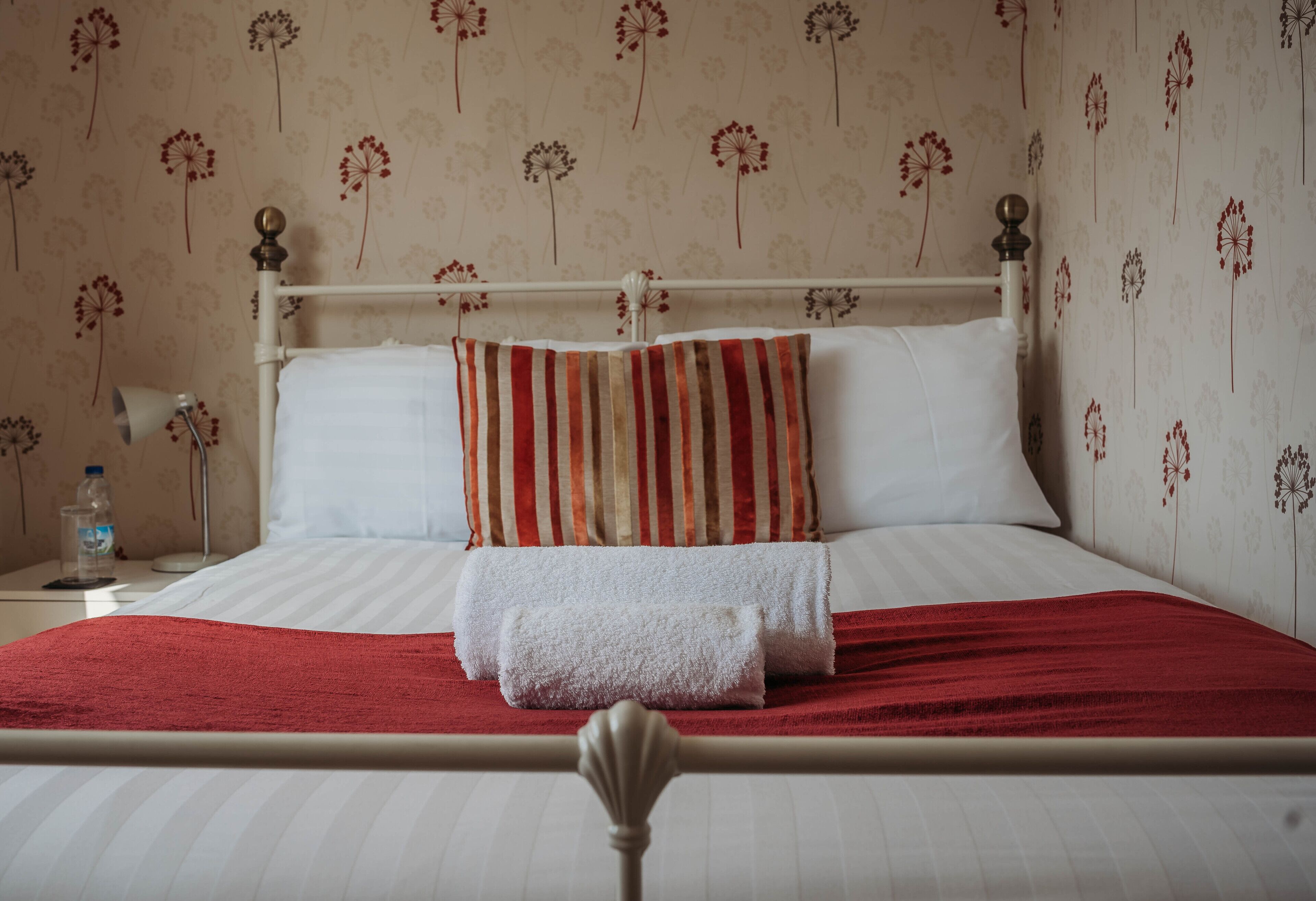 A neatly made bed with white linens, a red blanket, and striped pillows.