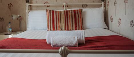 A neatly made bed with white linens, a red blanket, and striped pillows.