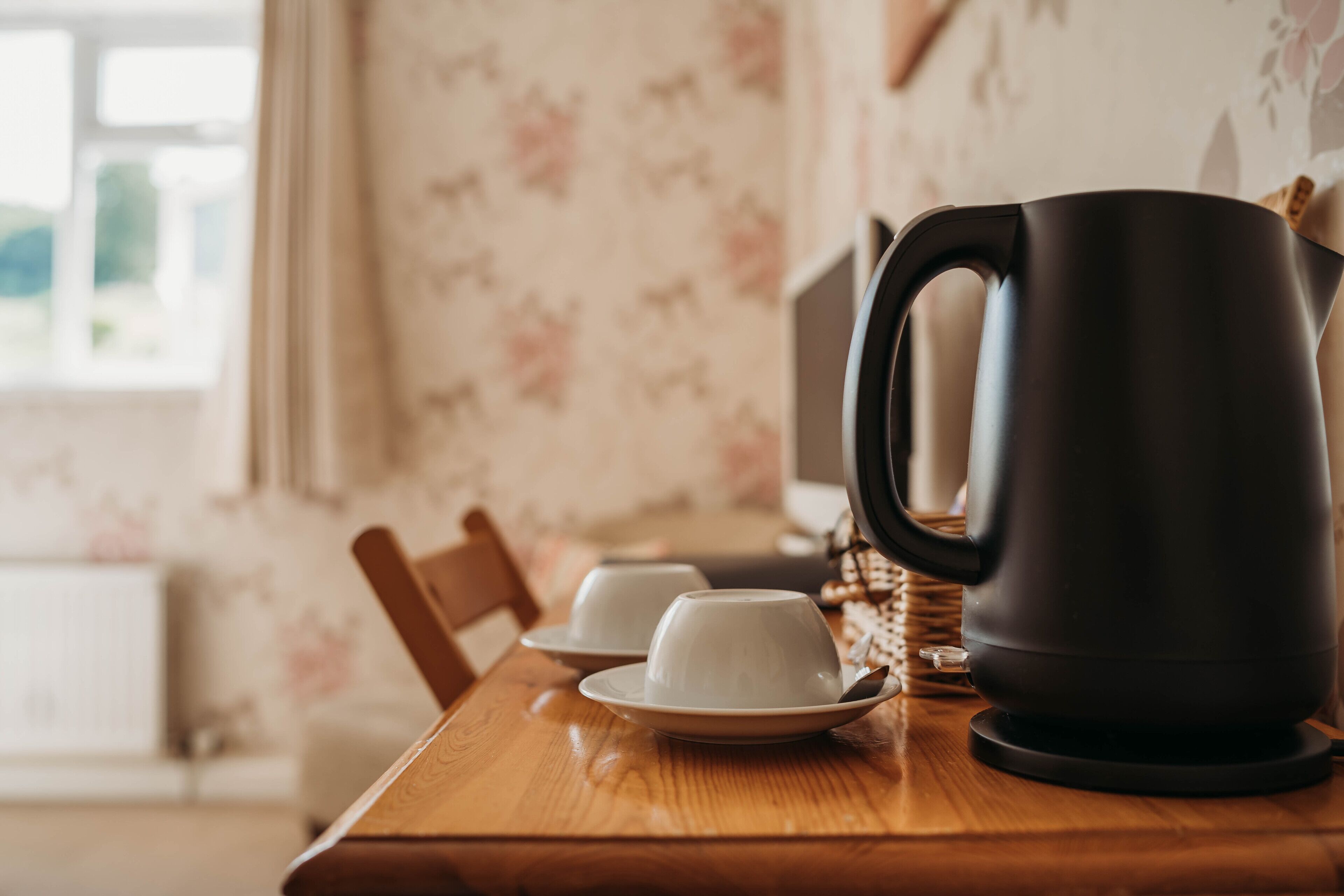 A wooden table with a black electric kettle, two white cups, and saucers.