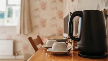 A wooden table with a black electric kettle, two white cups, and saucers.