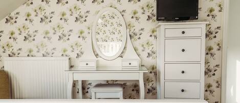 A bedroom with a white dresser, a vanity with a mirror, and a television on the wall.