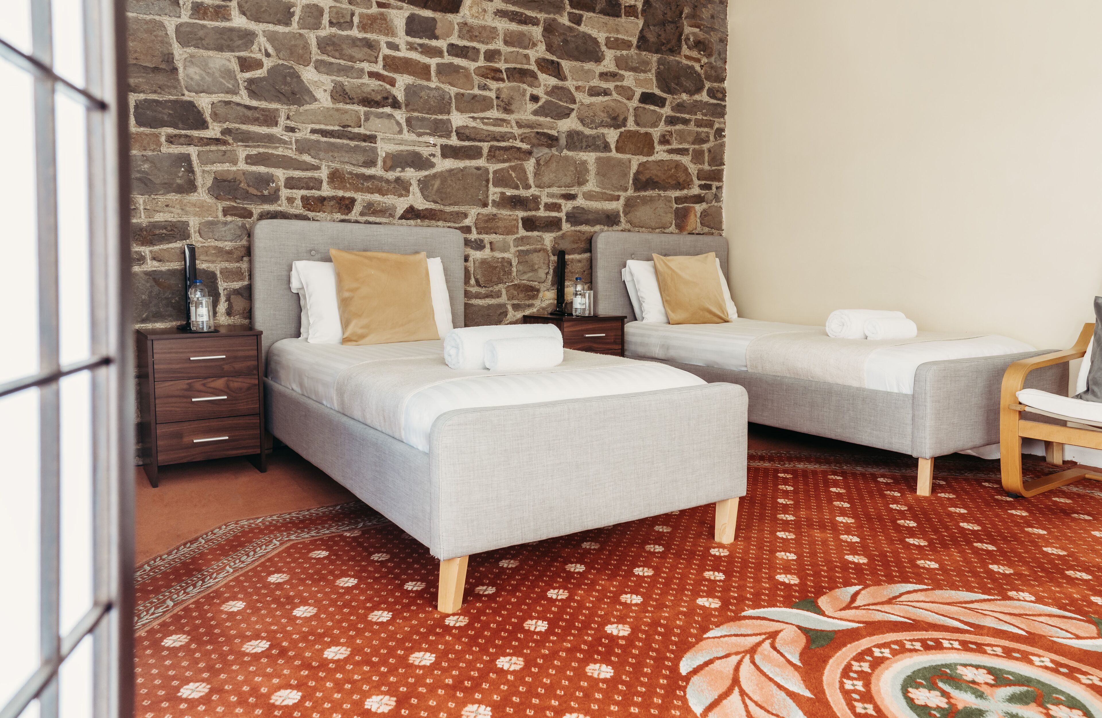 A room with two beds, a wooden nightstand, a chair, and a patterned carpet.