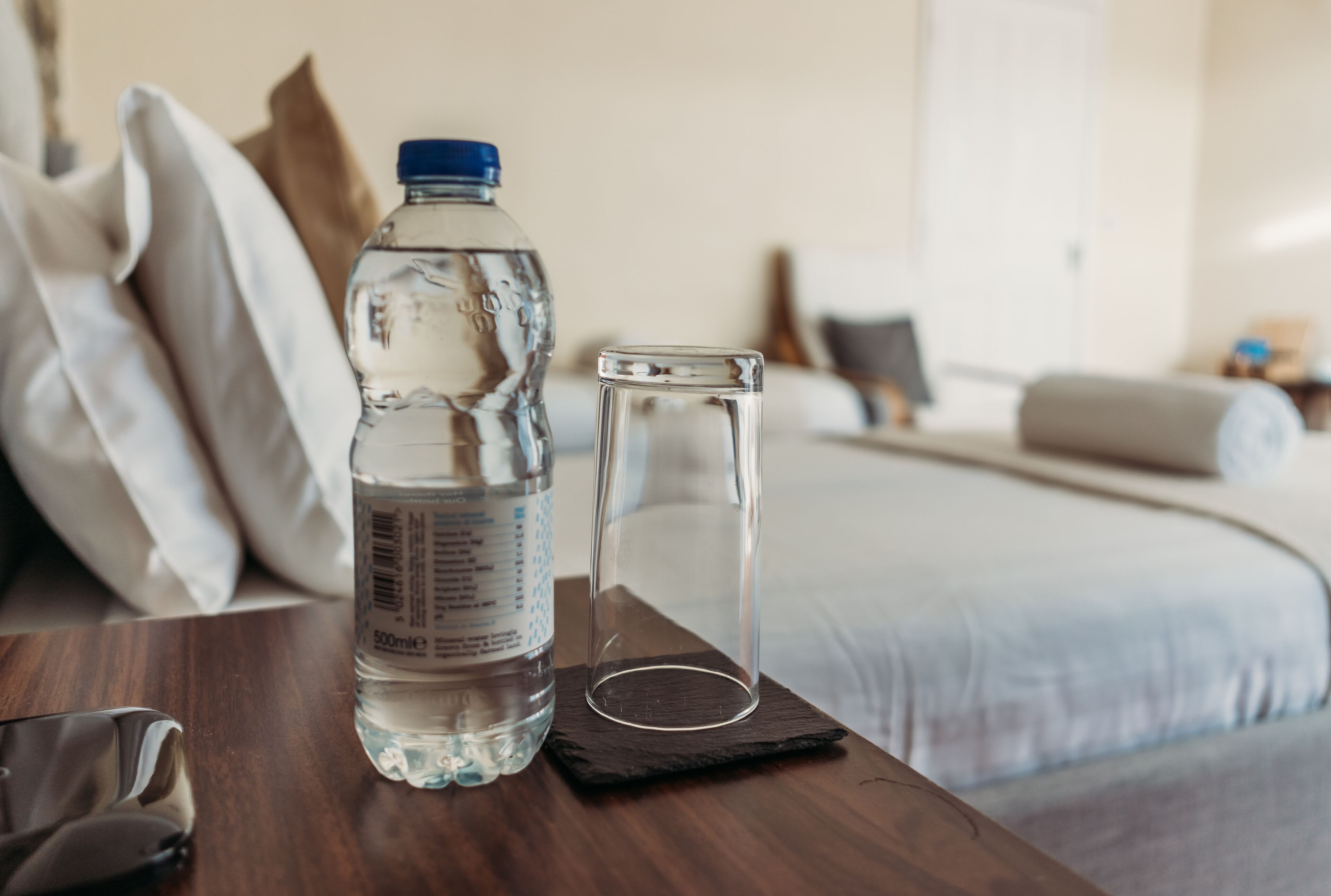 Una camera d'albergo con un tavolo in legno, una bottiglia d'acqua e un bicchiere di vetro.