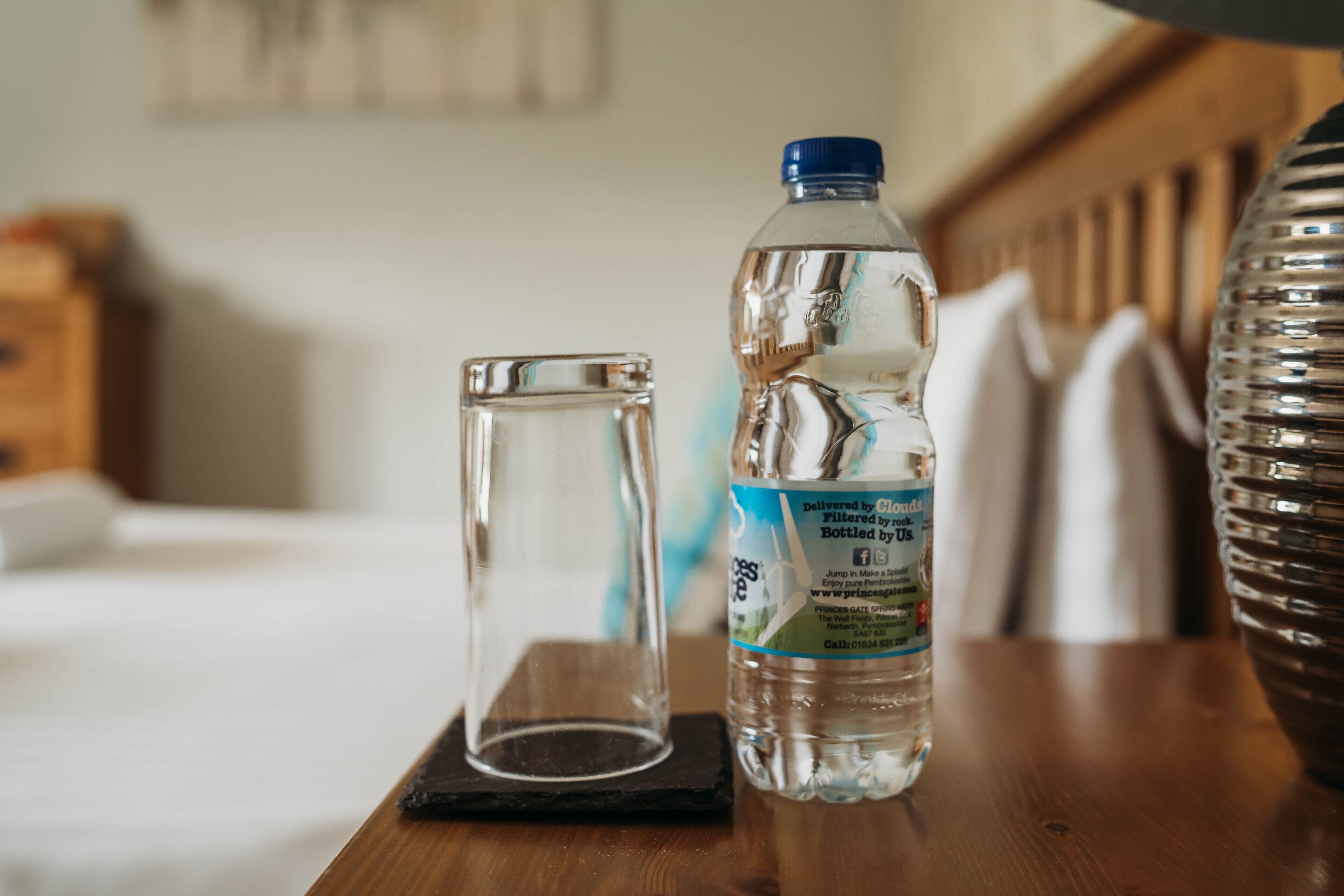 A clear glass bottle and a glass on a wooden table in a hotel room.
