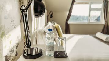 Een netjes ingerichte hotelkamer met een bureau, een waterfles, een glas en een lamp.