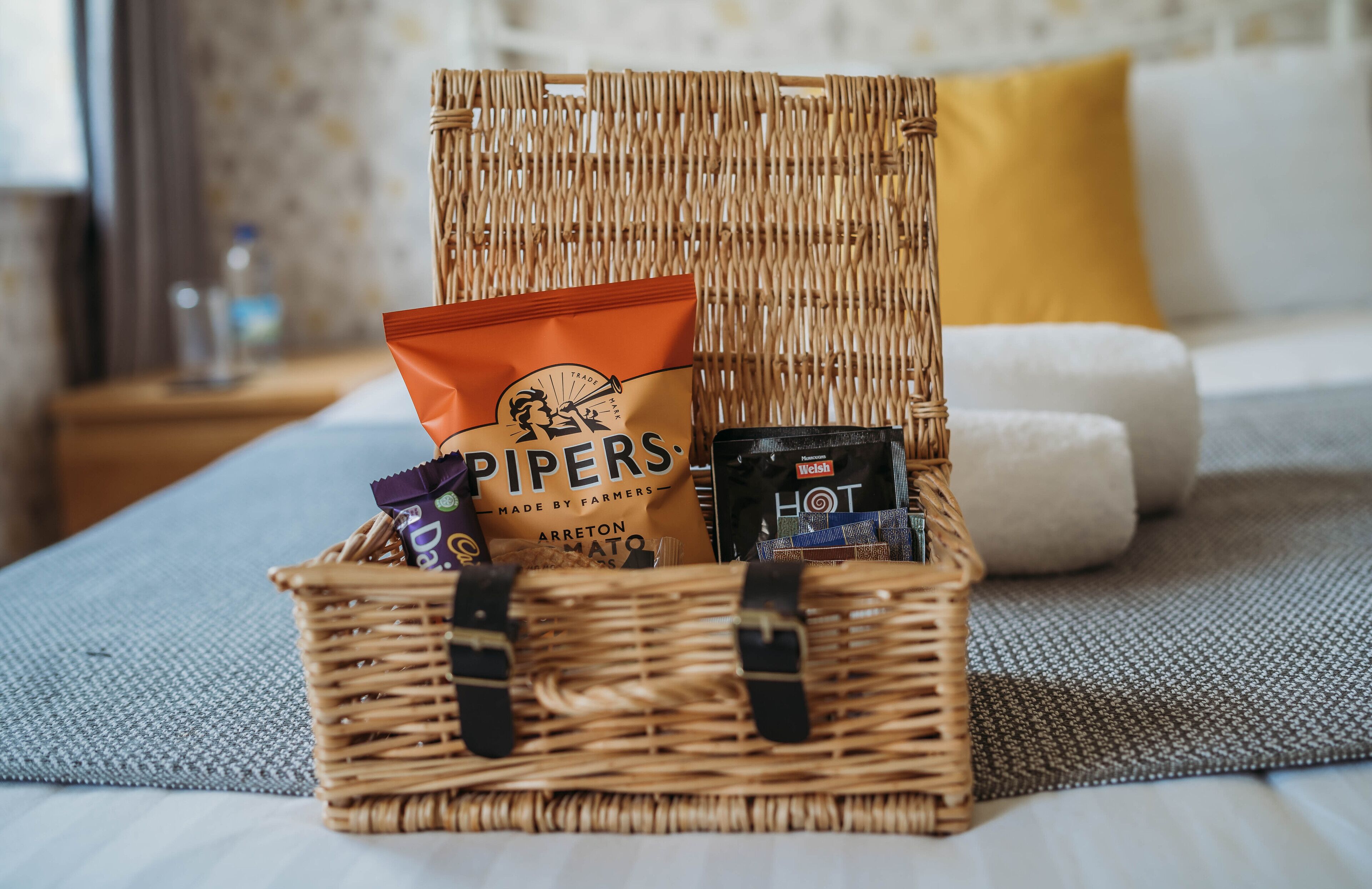 A wicker basket with snacks and a hot drink on a bed.