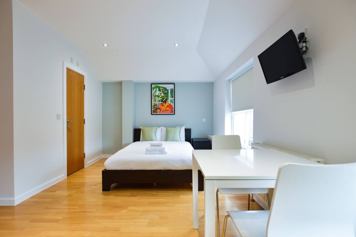 A modern bedroom with a bed, bedside table, and a TV mounted on the wall.