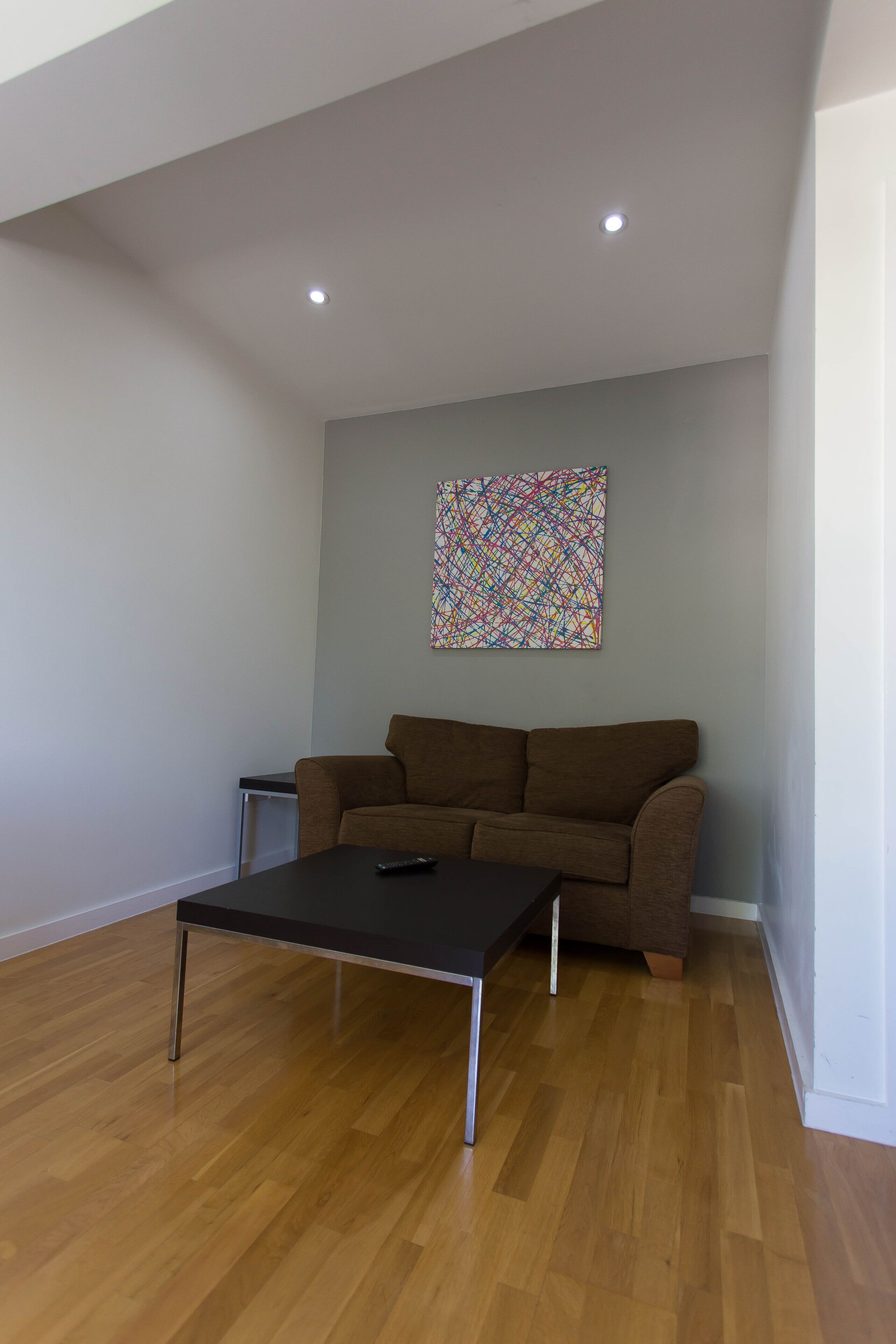 A living room with a brown sofa, a coffee table, and a colorful abstract painting on the wall.