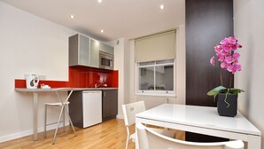A modern kitchen with white cabinets, a microwave, and a red countertop. There is a dining table with chairs and a potted orchid. - Princes Square Serviced Apartments by Concept Apartments (London)
