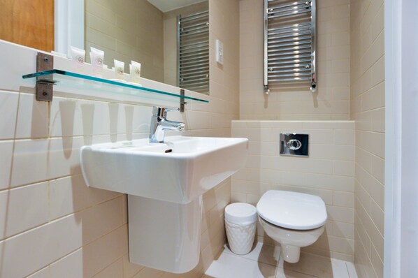 A modern bathroom with a white sink, glass shelf, and a toilet.