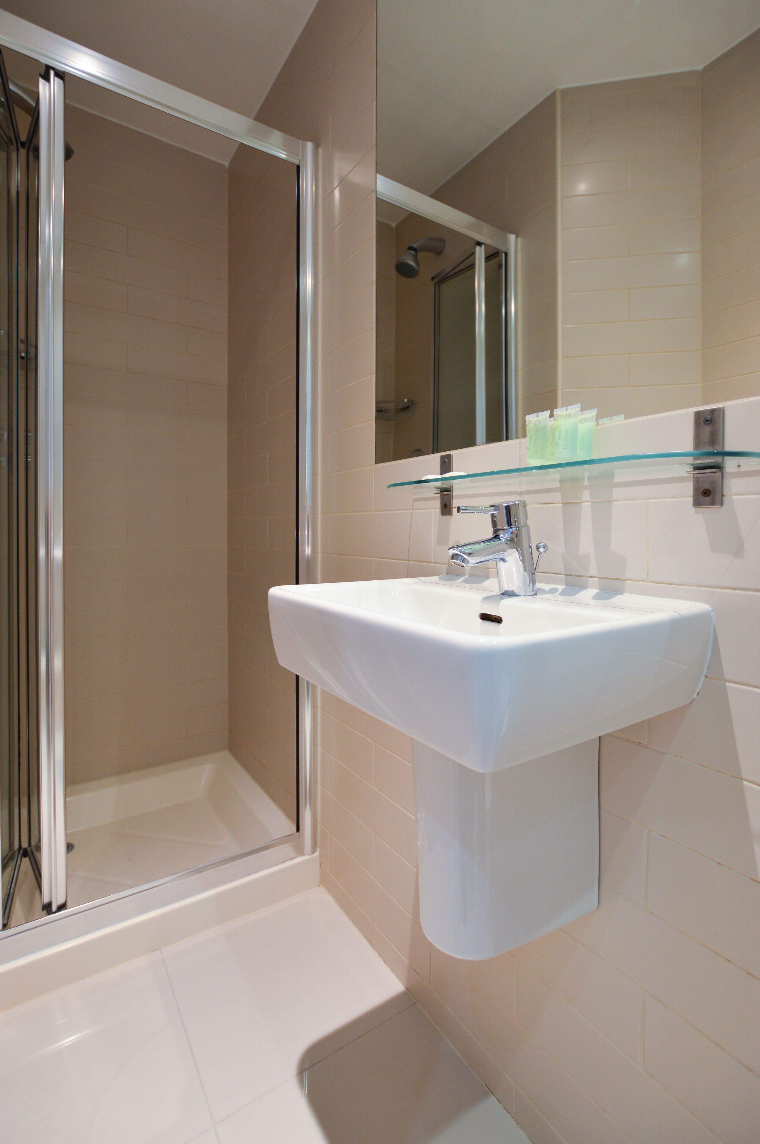 A bathroom with a glass-enclosed shower, a white sink, and a glass shelf above the sink.