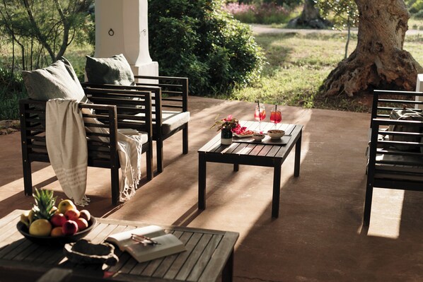 An outdoor seating area with wooden furniture, a table with drinks, and a bowl of fruit. - I Mulicchi (Specchia)