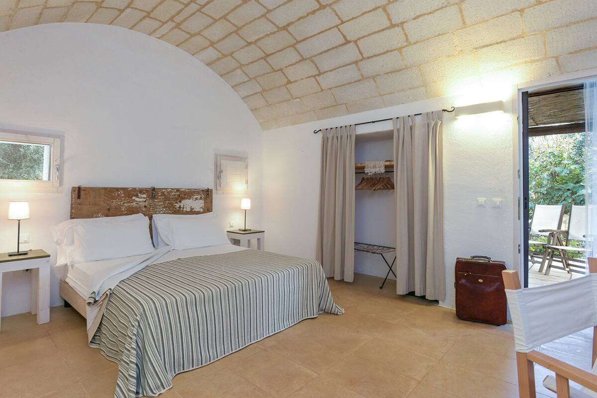 Un dormitorio con cama, mesitas de noche, armario y vistas al exterior.