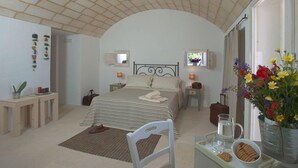 A bedroom with a bed, bedside tables, a chair, a window, and a vase with flowers. - I Mulicchi (Specchia)