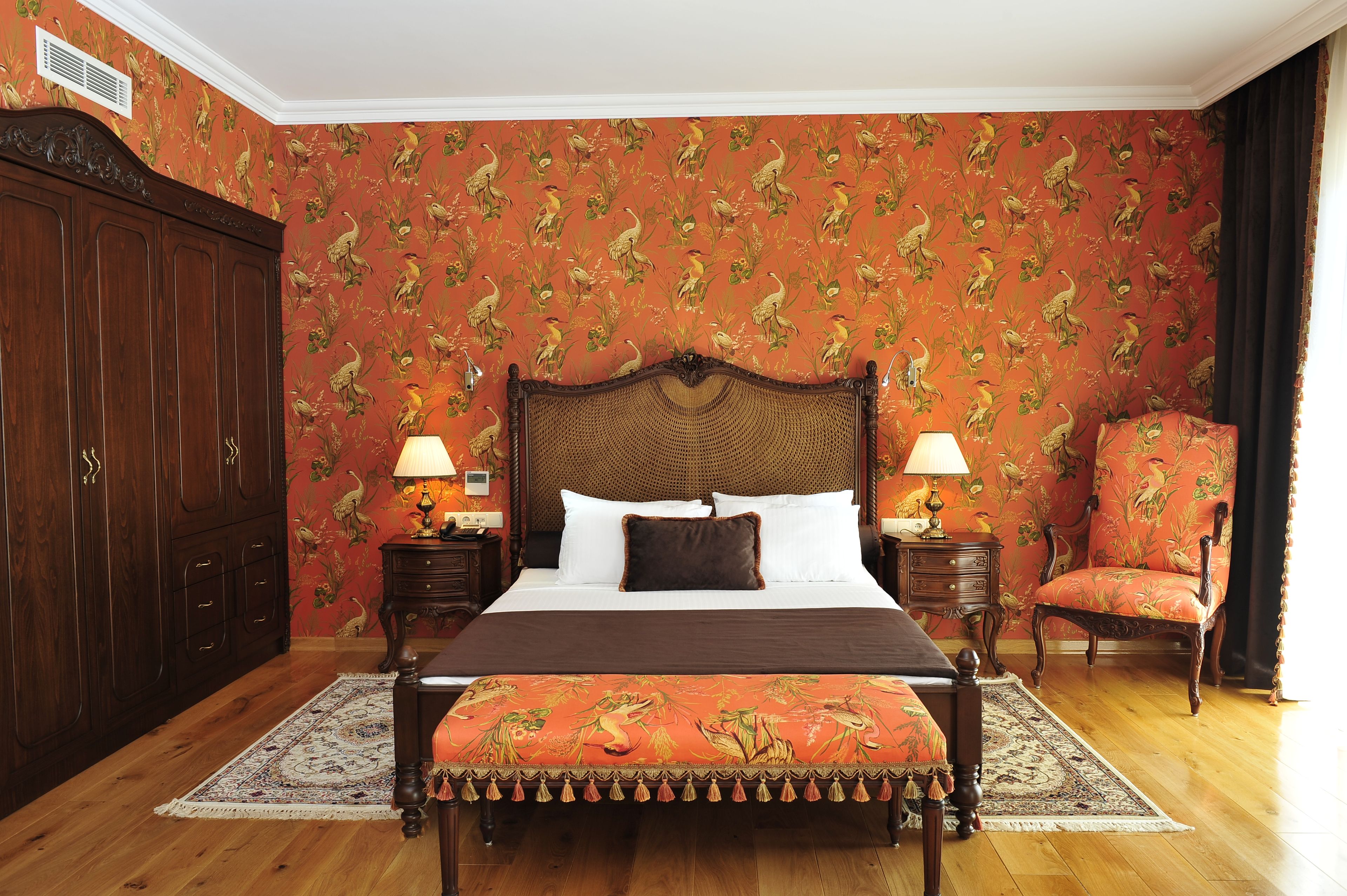 Un dormitorio con una cama grande, dos mesitas de noche con lámparas, un armario de madera, una silla y una alfombra estampada.