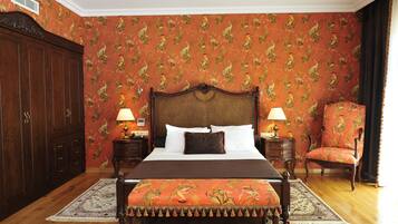 Un dormitorio con una cama grande, dos mesitas de noche con lámparas, un armario de madera, una silla y una alfombra estampada.