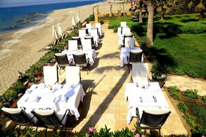 Un área de comedor al aire libre con mesas dispuestas para dos, con vista a la playa.