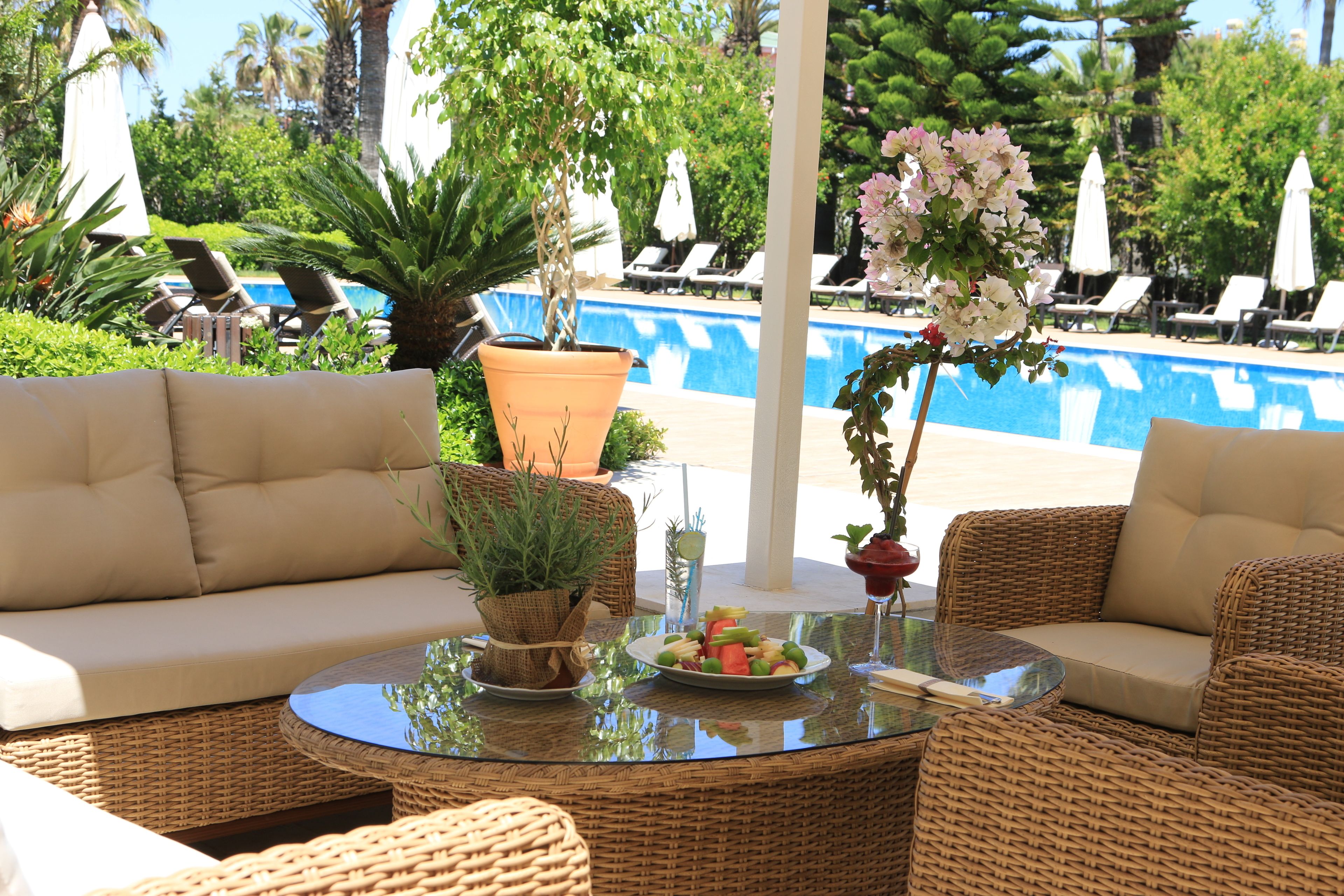 A poolside area with wicker furniture, a glass table, and a potted plant.