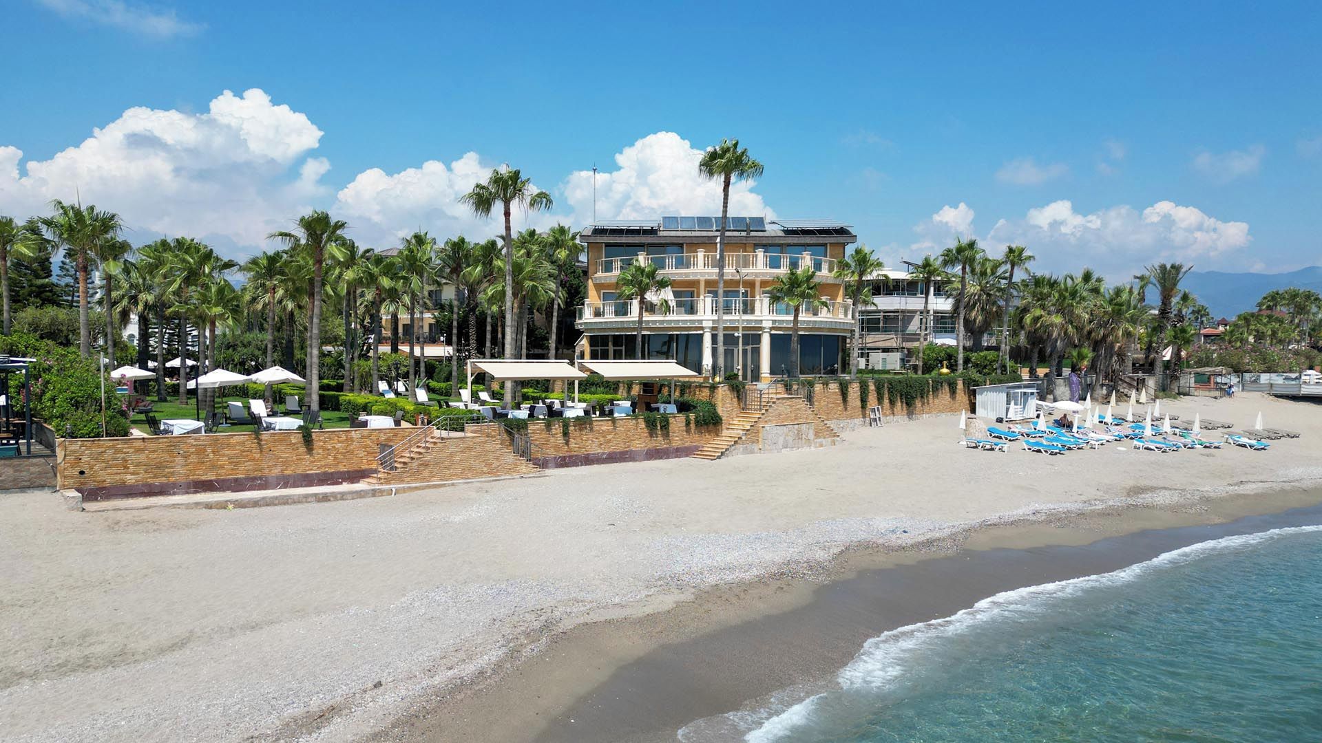 Un hotel frente a la playa con piscina, varias plantas y una playa con sombrillas.