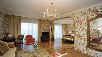 Un salón amplio con una araña, papel tapiz floral, un televisor y un espejo.