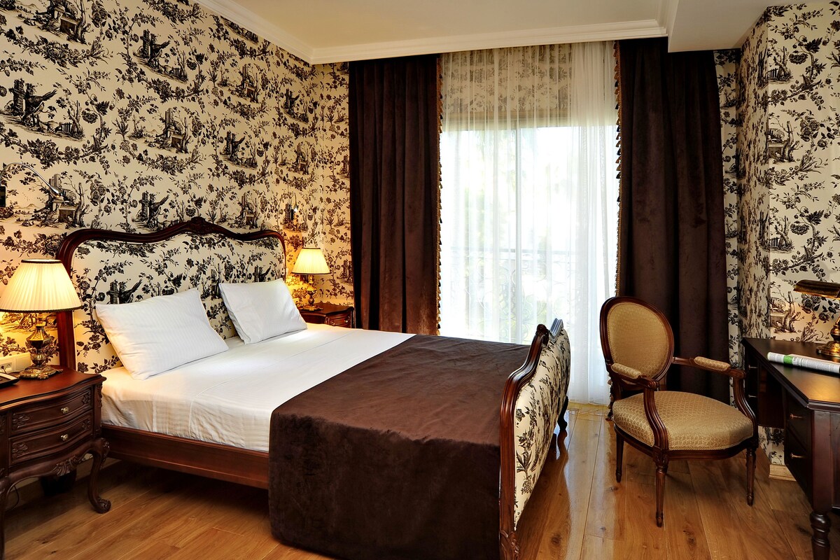 Una habitación de hotel con una cama grande, un sillón, un escritorio y una ventana con cortinas.
