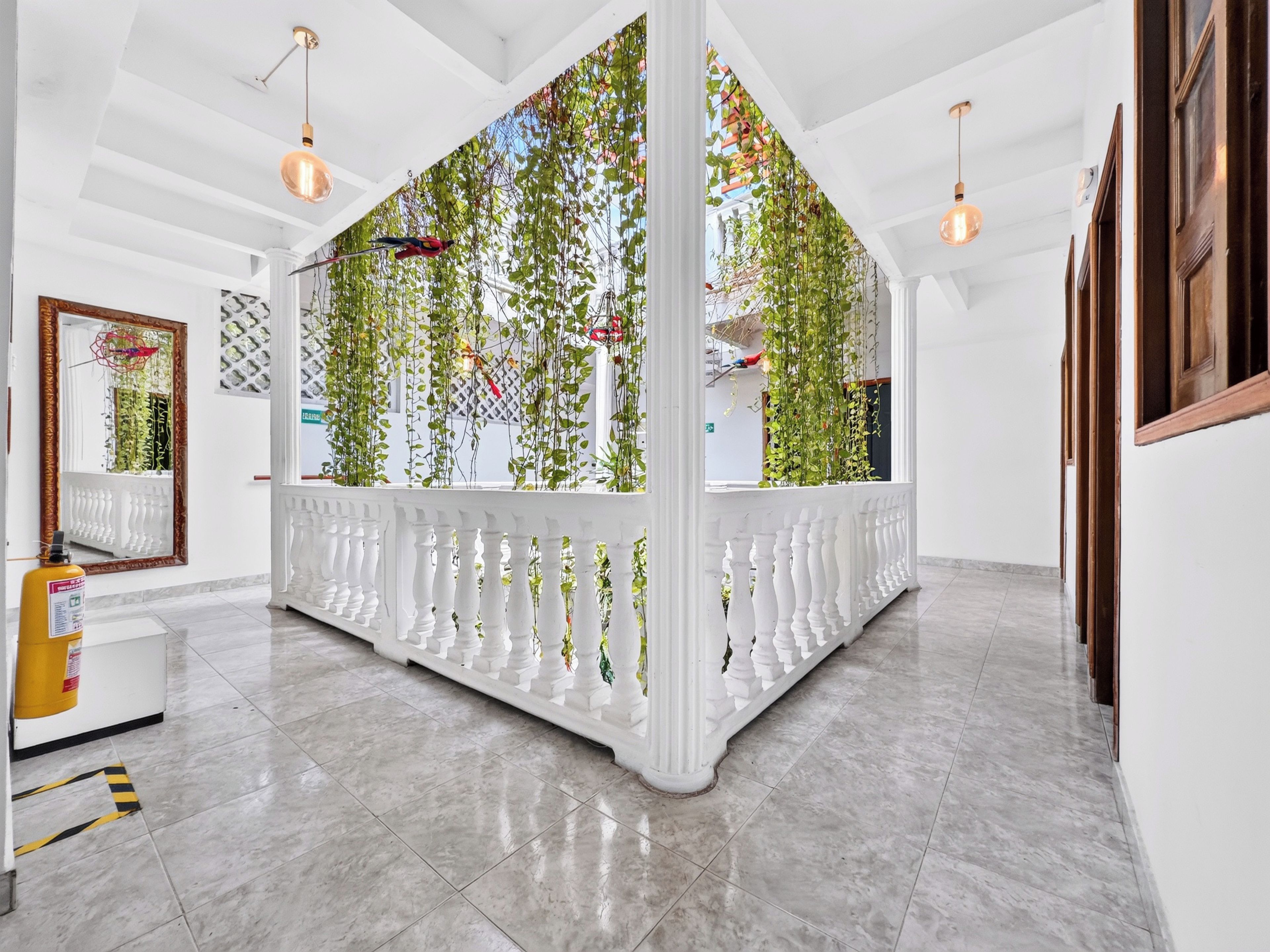 A hotel lobby with a white columned partition, hanging plants, and pendant lighting.